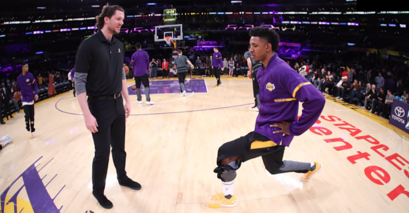 Sean Light coaching a Los Angeles Lakers player through a warmup lunge on court.